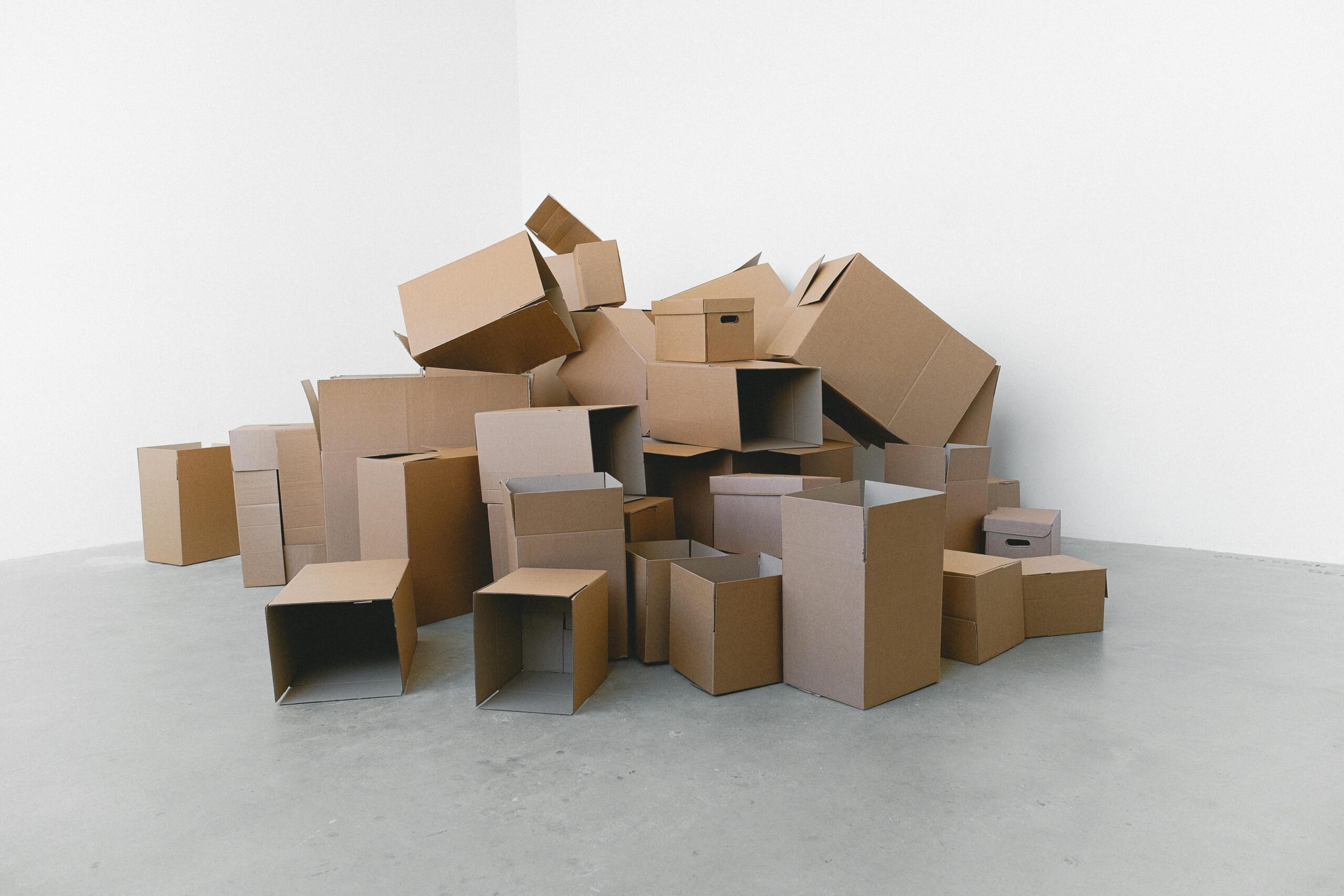 A pile of empty cardboard boxes arranged on a grey floor against a white wall, perfect for moving themes.